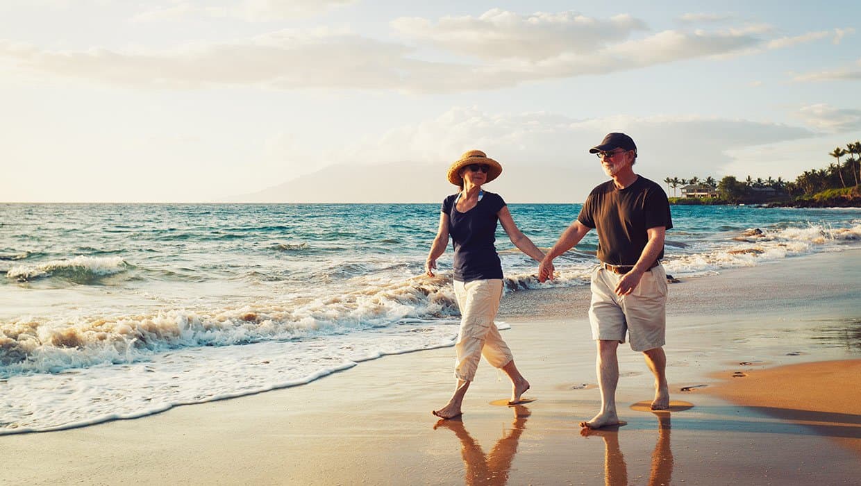 An older couple walking together along the shoreline at sunset